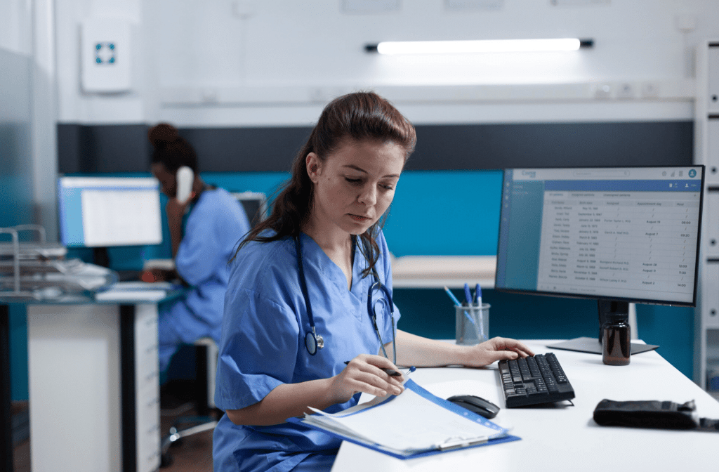 Nurse reviewing patient records on a computer at a clinic desk